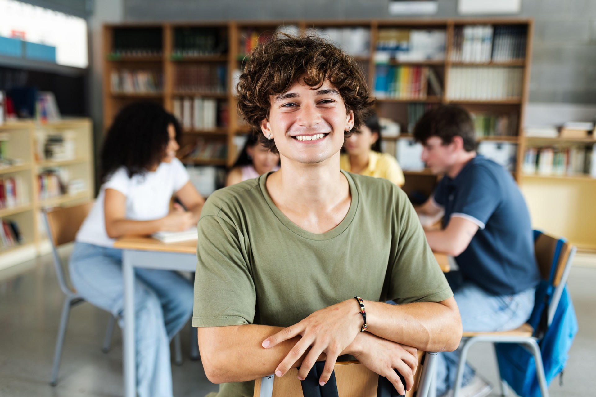 Junger Highschool-Schüler lächelt in der Bibliothek in die Kamera