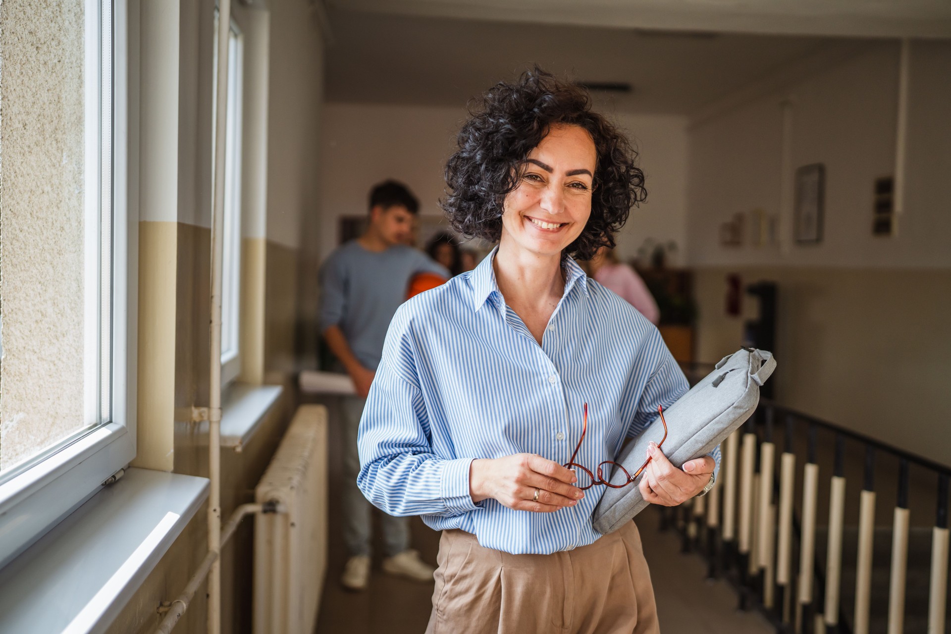 Reife Lehrerin geht selbstbewusst mit Handtasche durch den Schulflur